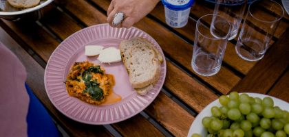 A casual outdoor dining table with bread, greens, and a side dish for brunch.