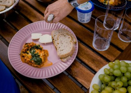 A casual outdoor dining table with bread, greens, and a side dish for brunch.