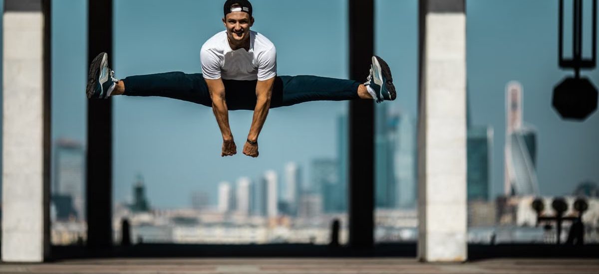Man performing a split jump on concrete, showcasing fitness and agility.